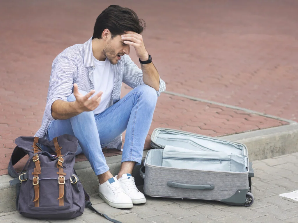 Sad man sitting at international airport with luggage What to Do If You Lose Your Passport in Foreign Countries